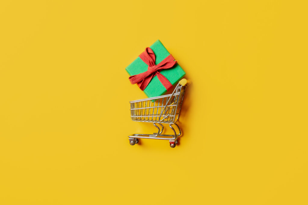 holiday gift box and supermarket cart on yellow background.