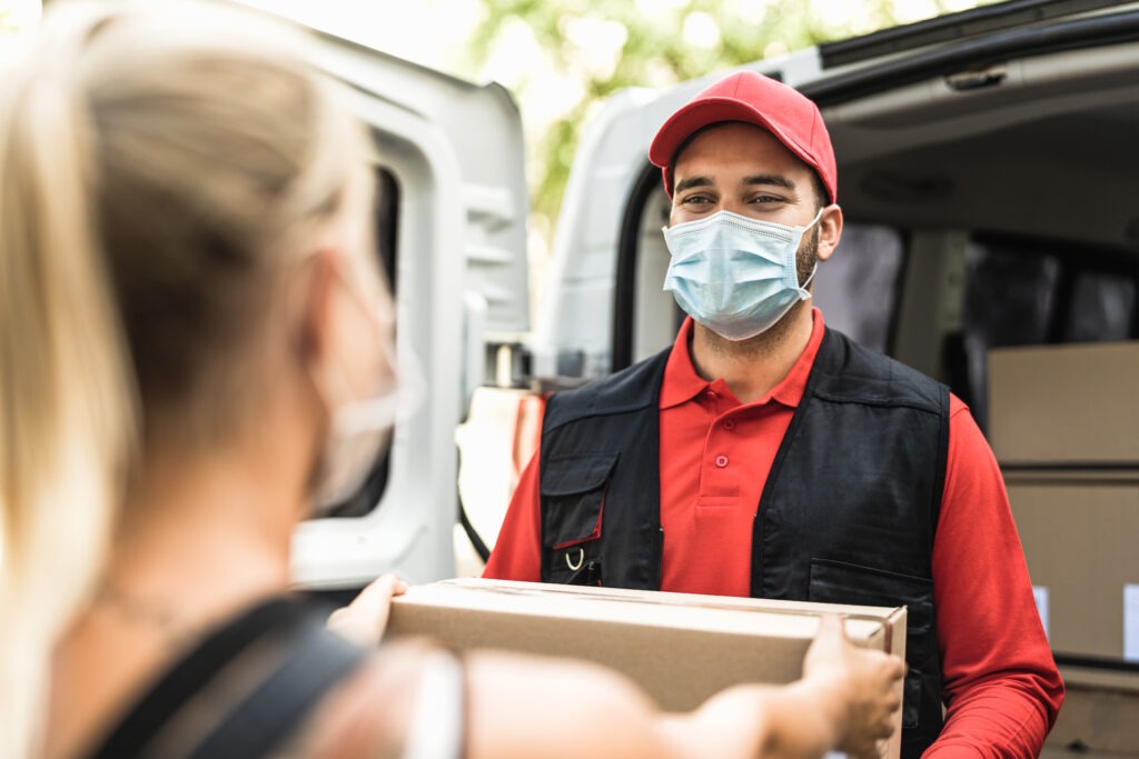 Delivery man at work wearing face mask - Young woman receiving