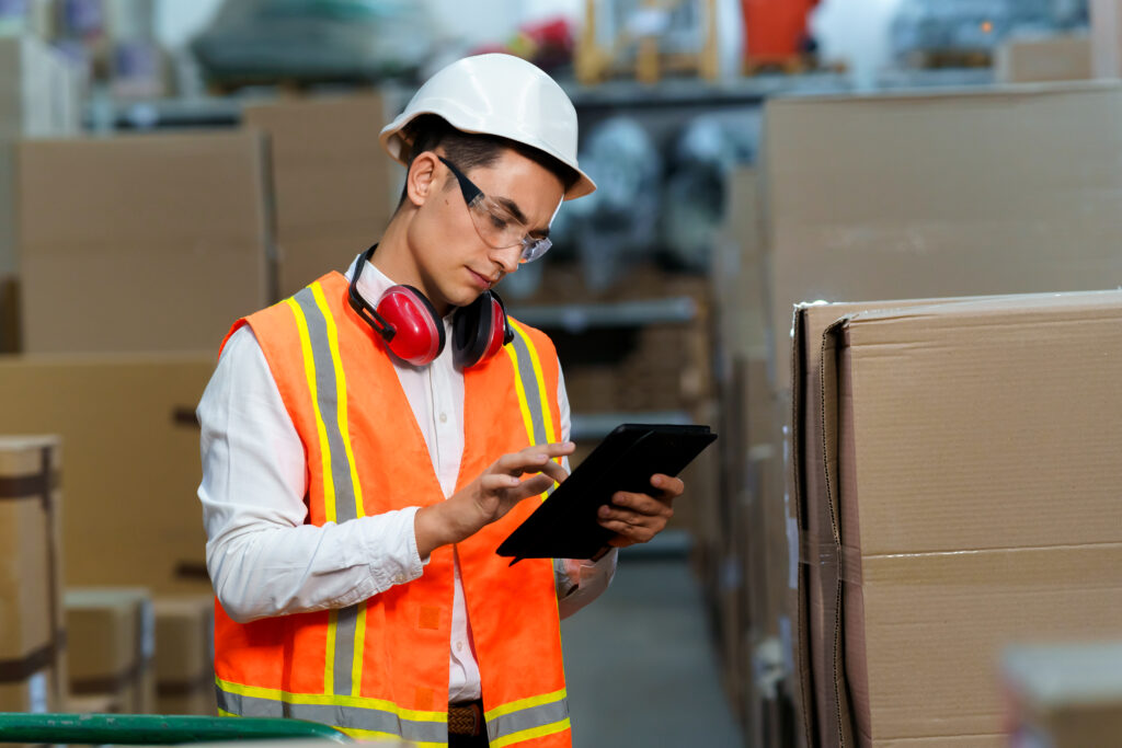 Young warehouse worker in safe clothes uses tablet